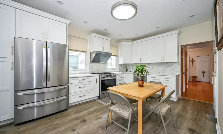 Kitchen with dark hardwood / wood-style flooring, white cabinetry, stainless steel appliances, and exhaust hood