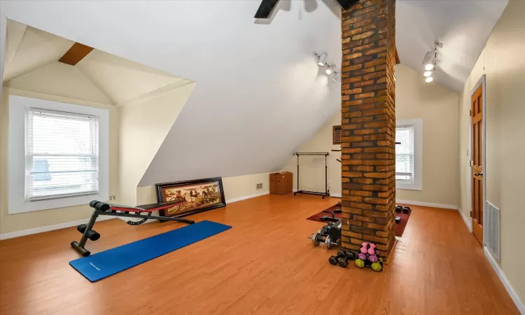 Exercise area featuring wood-type flooring, decorative columns, a wealth of natural light, and lofted ceiling