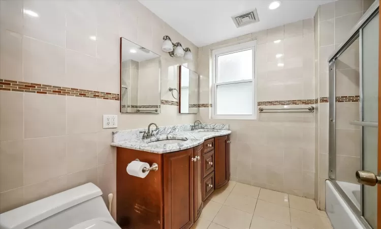 Full bathroom featuring tile patterned floors, bath / shower combo with glass door, toilet, vanity, and tile walls