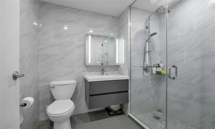 Bathroom with walk in shower, tile patterned floors, toilet, vanity, and tile walls