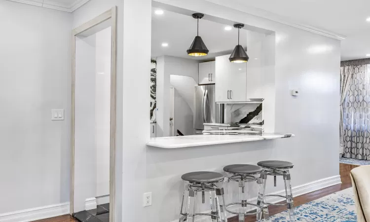 Kitchen with stainless steel fridge, dark hardwood / wood-style flooring, crown molding, decorative light fixtures, and white cabinets