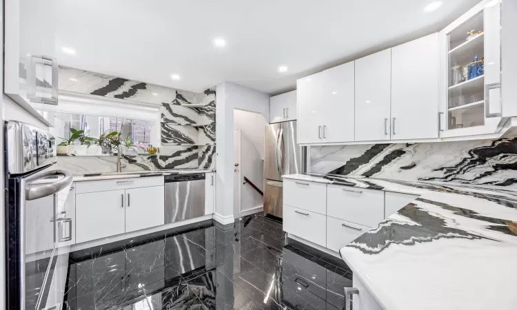 Kitchen featuring white cabinets, decorative backsplash, light stone countertops, and appliances with stainless steel finishes