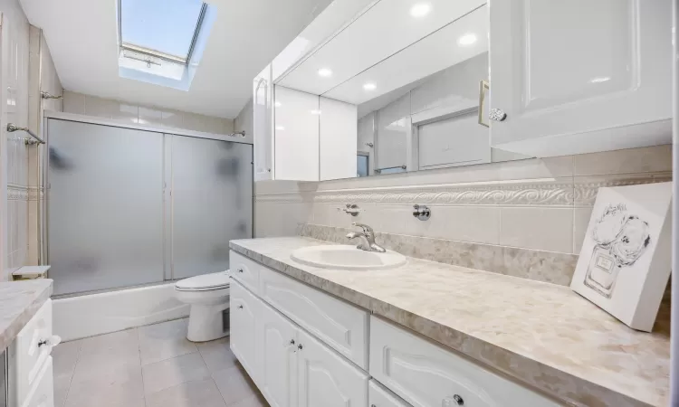 Full bathroom with a skylight, backsplash, toilet, shower / bath combination with glass door, and vanity