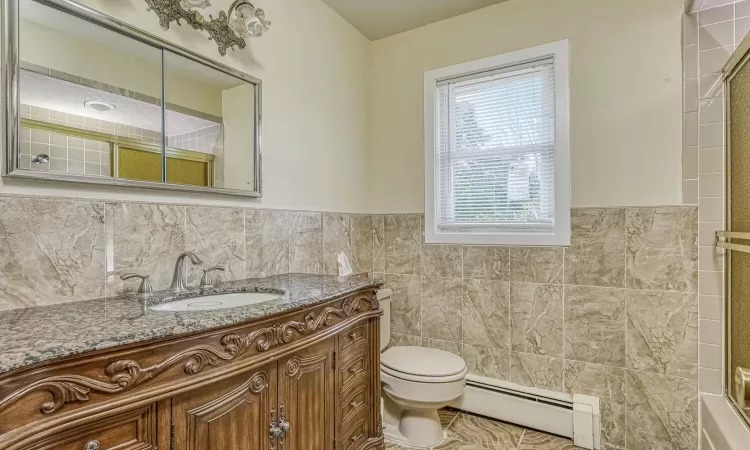 Bathroom with vanity, toilet, tile walls, and a baseboard heating unit