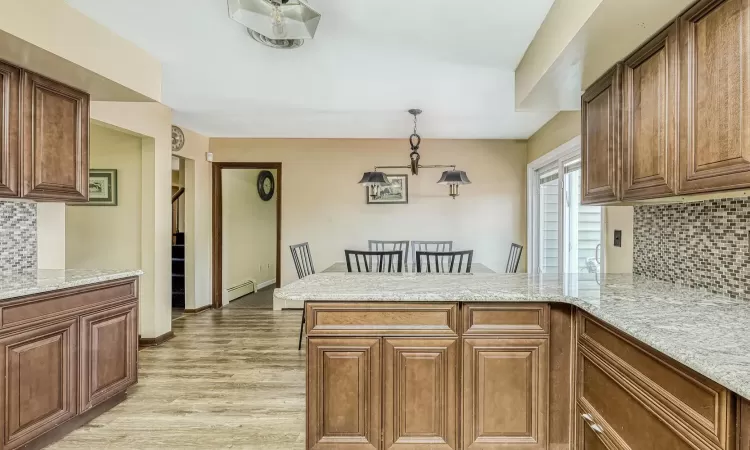 Kitchen with kitchen peninsula, decorative backsplash, light stone counters, pendant lighting, and a baseboard radiator