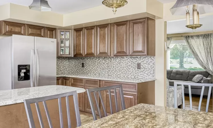 Kitchen featuring white refrigerator with ice dispenser, decorative backsplash, and light stone counters