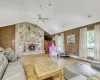 Living room featuring vaulted ceiling, ceiling fan, wooden walls, hardwood / wood-style floors, and a stone fireplace