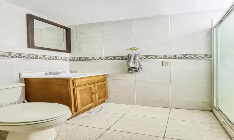 Bathroom with vanity, tile patterned flooring, toilet, tile walls, and a shower with shower door