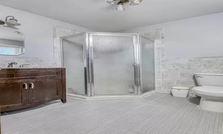 Bathroom featuring an enclosed shower, vanity, tile walls, tile patterned flooring, and toilet