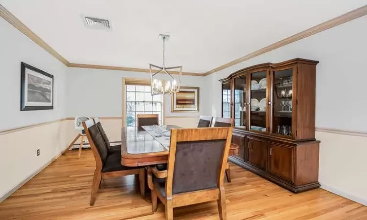 Dining area with a chandelier, light hardwood / wood-style flooring, baseboard heating, and ornamental molding