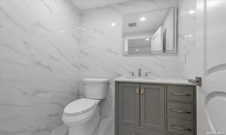 Bathroom featuring vanity, tile walls, and toilet