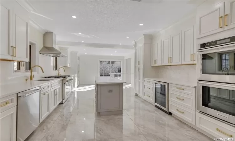 Kitchen with sink, stainless steel appliances, white cabinetry, and wall chimney range hood (STAGED)