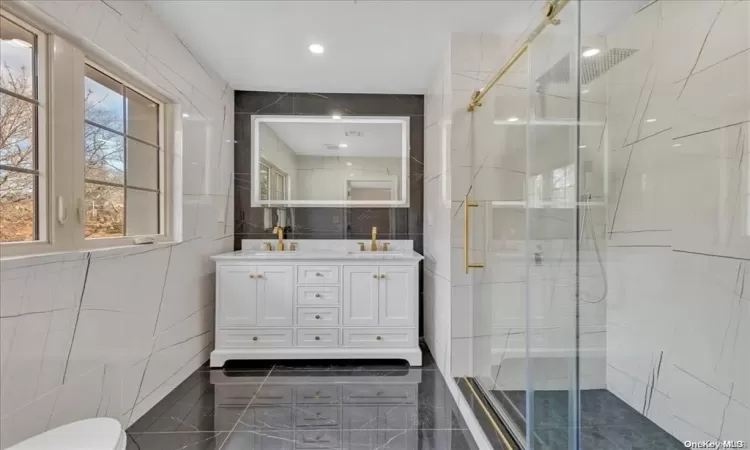 Bathroom with vanity, an enclosed shower, and tile walls