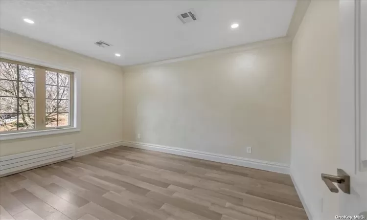 Empty room featuring crown molding, light hardwood / wood-style flooring, and a baseboard radiator