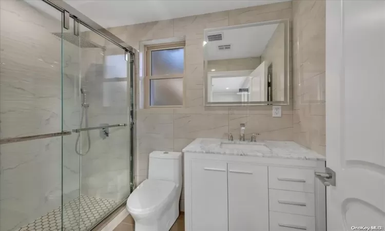 Bathroom with vanity, a shower with shower door, tile walls, and toilet