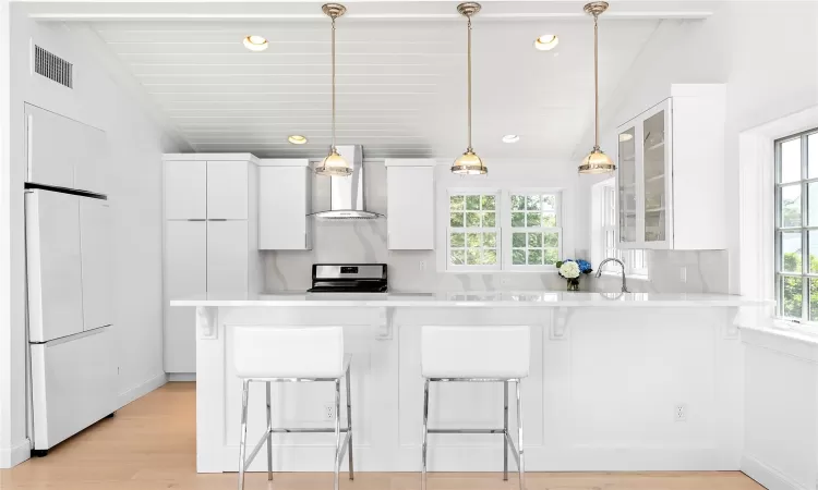 Kitchen with lofted ceiling, white cabinetry, wall chimney range hood, and fridge