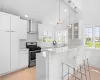 Kitchen featuring stainless steel gas range oven, a breakfast bar, wall chimney range hood, lofted ceiling with beams, and white cabinetry