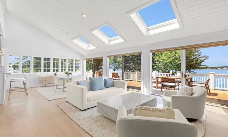 Living room with a skylight, high vaulted ceiling, light hardwood / wood-style floors, a water view, and wood ceiling