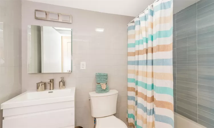 Full bathroom with shower / bath combo with shower curtain, vanity, tile walls, and toilet