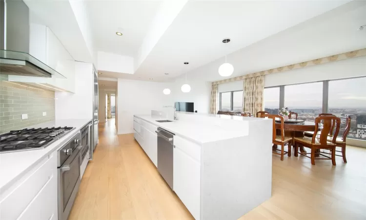 Kitchen with decorative light fixtures, stainless steel appliances, wall chimney range hood, and white cabinetry