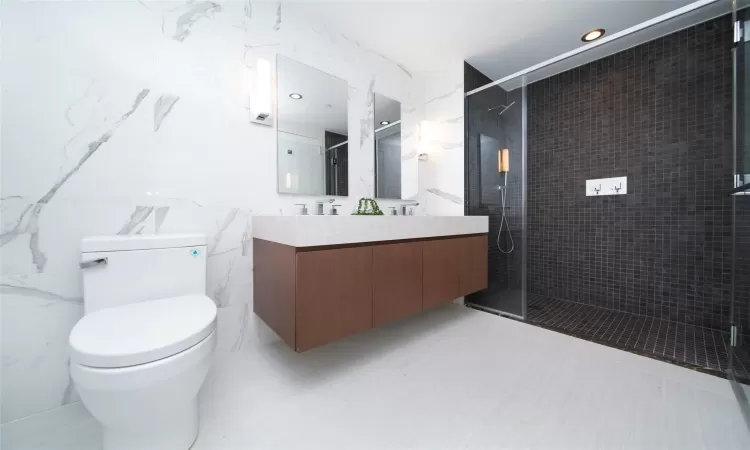 Bathroom featuring toilet, a shower with shower door, tile walls, and vanity