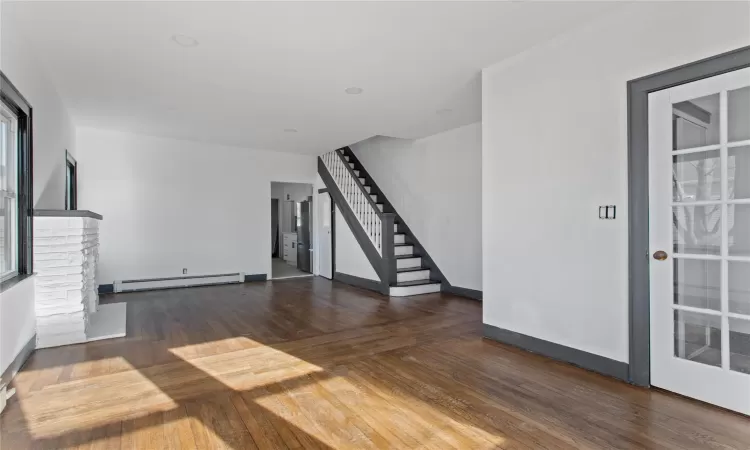 Unfurnished living room featuring dark wood-type flooring, a stone fireplace, and a baseboard radiator