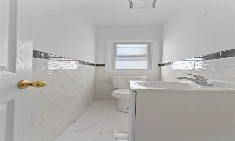 Bathroom featuring tile walls, toilet, and vanity