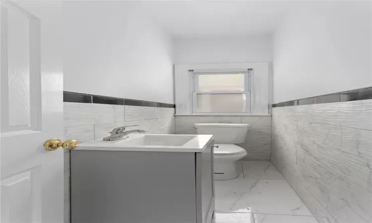 Bathroom with toilet, vanity, and tile walls