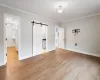 Unfurnished bedroom with ensuite bath, a barn door, light hardwood / wood-style flooring, and ornamental molding