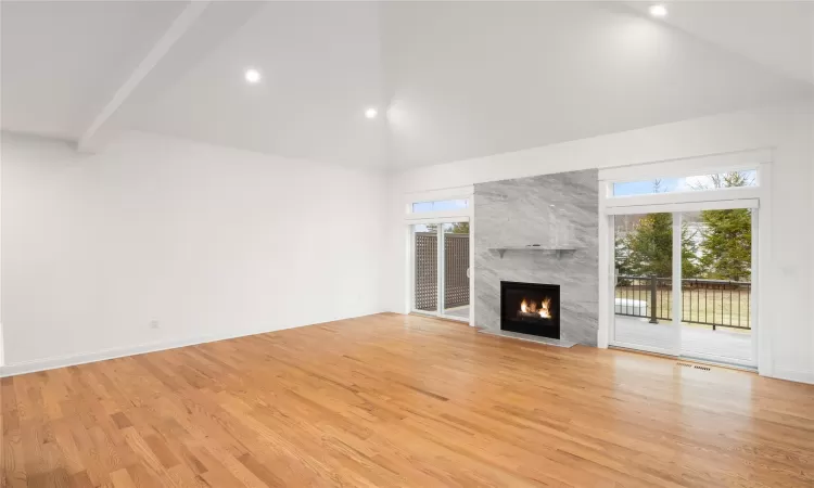 Unfurnished living room featuring light hardwood / wood-style floors, beamed ceiling, high vaulted ceiling, and a fireplace