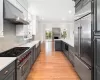 Kitchen with white cabinetry, built in appliances, wall chimney exhaust hood, sink, and light hardwood / wood-style flooring