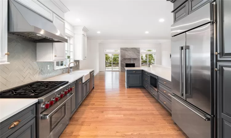 Kitchen with white cabinetry, built in appliances, wall chimney exhaust hood, sink, and light hardwood / wood-style flooring