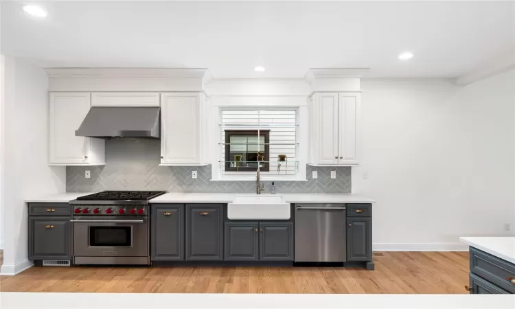 Kitchen featuring wall chimney exhaust hood, light wood-type flooring, white cabinetry, appliances with stainless steel finishes, and sink