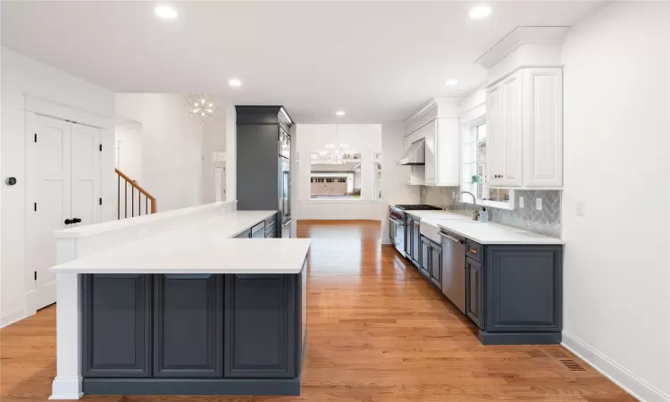 Kitchen with stainless steel appliances, ventilation hood, kitchen peninsula, a notable chandelier, and white cabinets