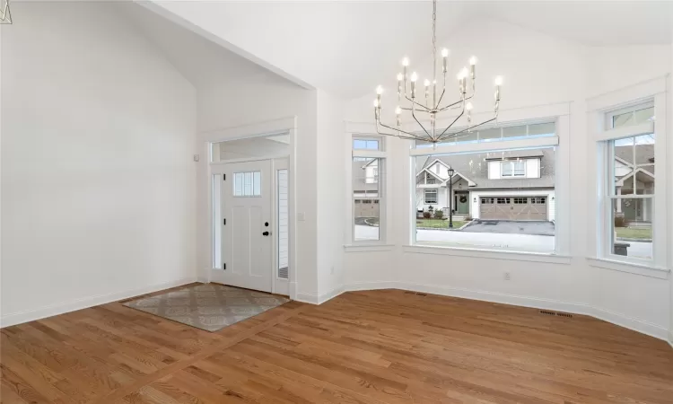 Entryway with a notable chandelier, vaulted ceiling, a wealth of natural light, and wood-type flooring