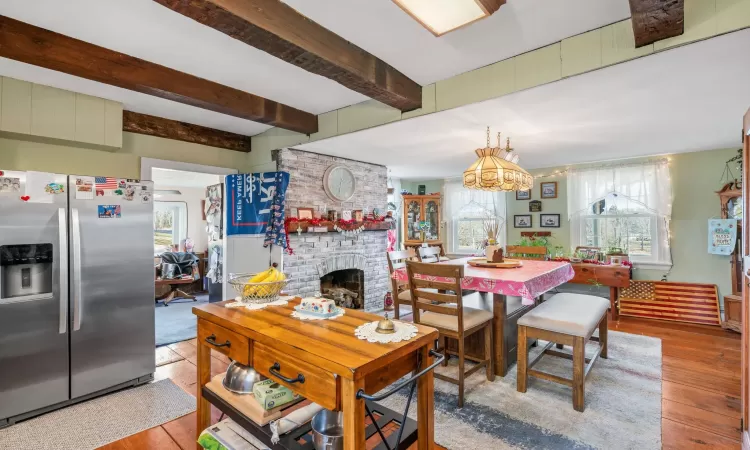 Dining room with beam ceiling, an inviting chandelier, light hardwood / wood-style floors, and a brick fireplace