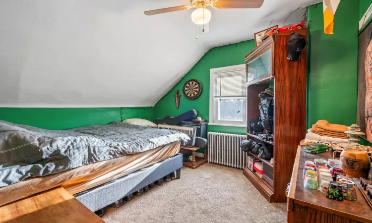 Carpeted bedroom featuring radiator, ceiling fan, and vaulted ceiling