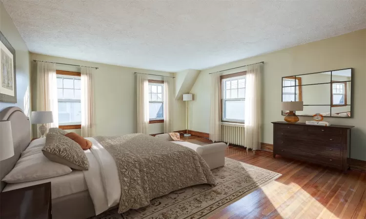 Staged - Bedroom featuring hardwood / wood-style flooring, a textured ceiling, radiator, and multiple windows