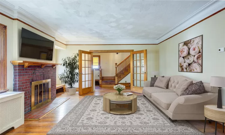 Staged - Living room with radiator, french doors, hardwood / wood-style flooring, ornamental molding, and a fireplace