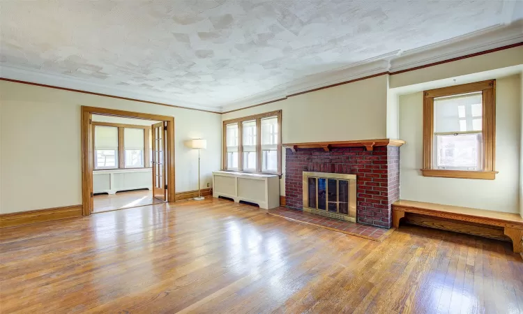 Unfurnished living room featuring hardwood / wood-style floors, crown molding, radiator, and a brick fireplace