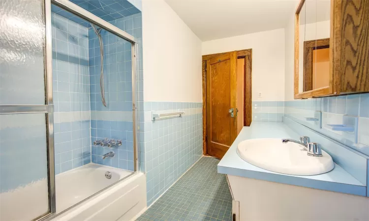 Bathroom with vanity, tile patterned floors, tile walls, and bath / shower combo with glass door