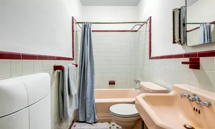 Full bathroom featuring toilet, sink, shower / bathtub combination with curtain, and tile walls