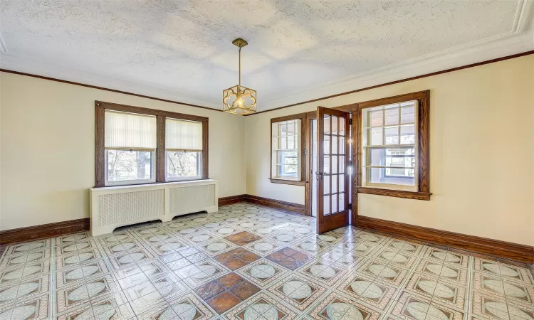 Empty room with a wealth of natural light, a textured ceiling, radiator, and an inviting chandelier