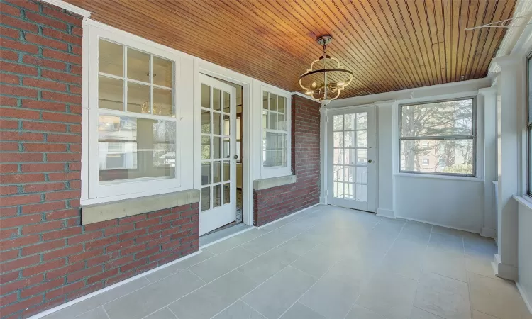 Unfurnished sunroom with wood ceiling and a notable chandelier