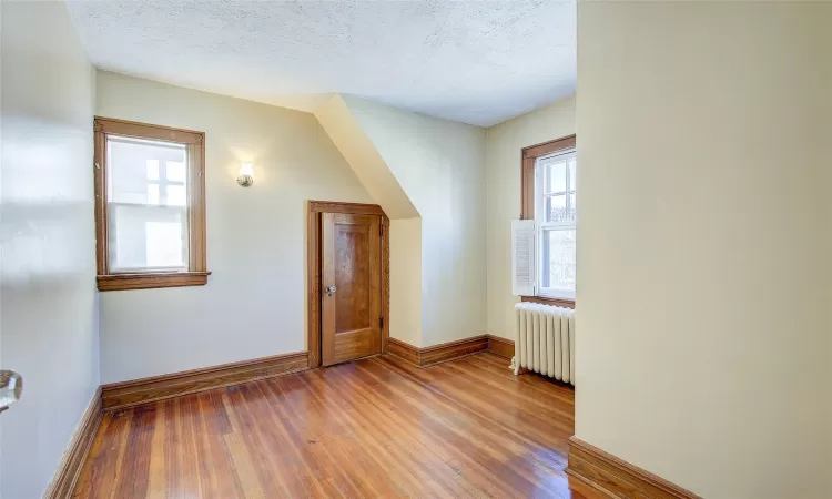 Bonus room with hardwood / wood-style floors, radiator heating unit, and a textured ceiling