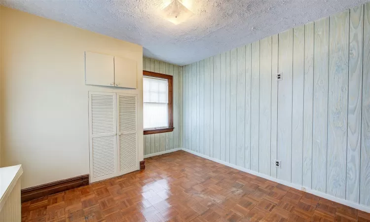 Unfurnished bedroom with dark parquet floors, a textured ceiling, and a closet