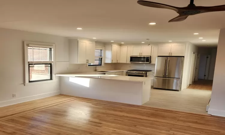 Kitchen featuring premium appliances, kitchen peninsula, light wood-type flooring, and white cabinetry