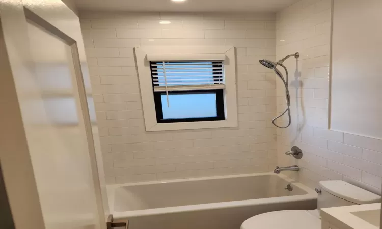 Full bathroom featuring toilet, tiled shower / bath, tile walls, and vanity