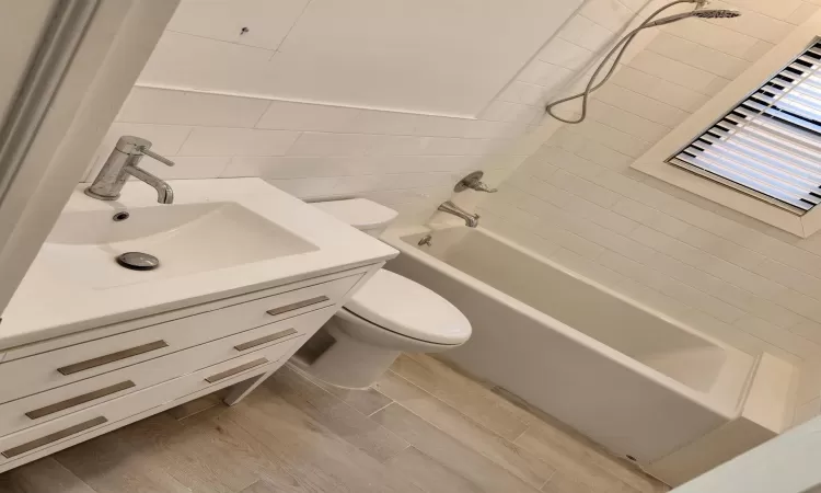 Full bathroom featuring toilet, tile walls, tiled shower / bath combo, wood-type flooring, and vanity