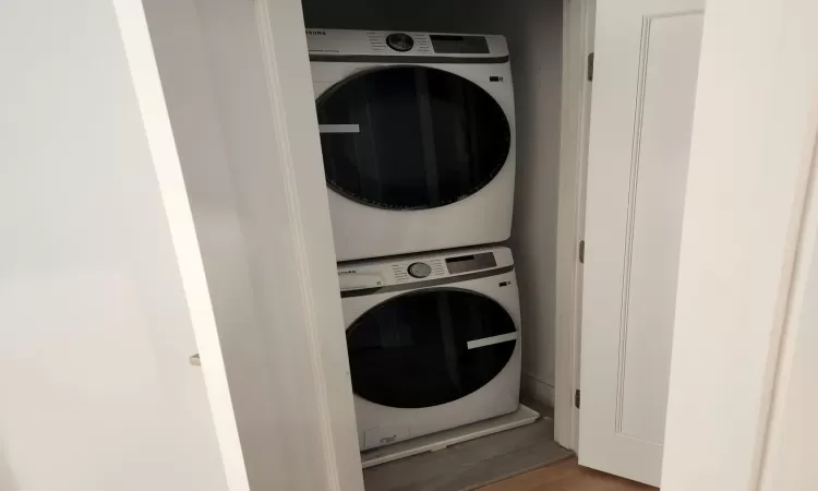 Clothes washing area with stacked washer / drying machine and hardwood / wood-style flooring